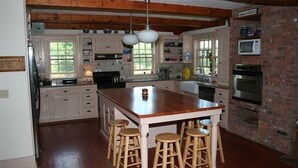 Een keuken met een groot schiereiland, houten krukken, witte kasten, een accentmuur van baksteen en moderne apparatuur.