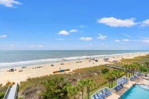 Une vue sur la plage, avec une piscine, des palmiers et un ciel dégagé.