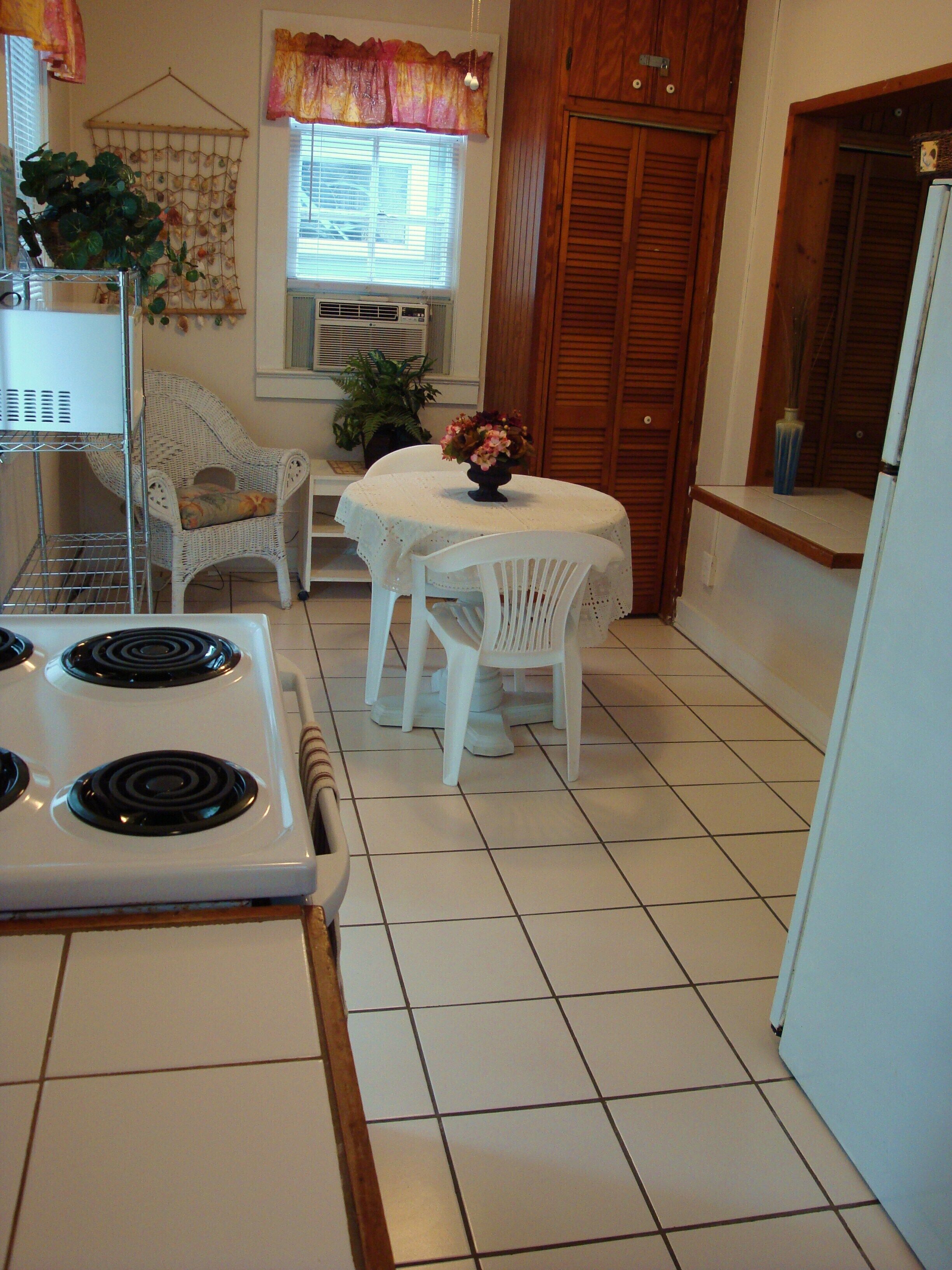 A kitchen with white appliances, a dining table with chairs, and a window with blinds.