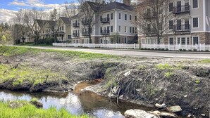 Una hilera de casas de varios pisos con valla blanca, un pequeño arroyo y cielo despejado.
