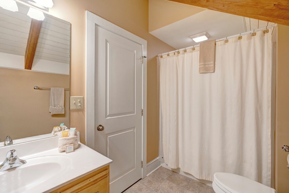 Une salle de bain avec un lavabo blanc, un miroir et des toilettes. Il y a un rideau de douche et une serviette accrochée au mur.