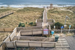 A wooden boardwalk leading to a beach area with a sign indicating 'Welcome to Kure Beach' and '343 S. Fort Fisher Blvd.'