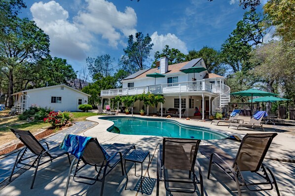 A two-story house with a swimming pool, outdoor seating, and a covered patio area.