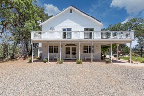 A white two-story house with a covered porch, multiple windows, and a gravel driveway.