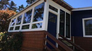 Una casa con un amplio ventanal, una terraza de madera y fachada azul.
