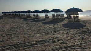 Una spiaggia con file di lettini e ombrelloni, una battigia sabbiosa e l'oceano sullo sfondo.