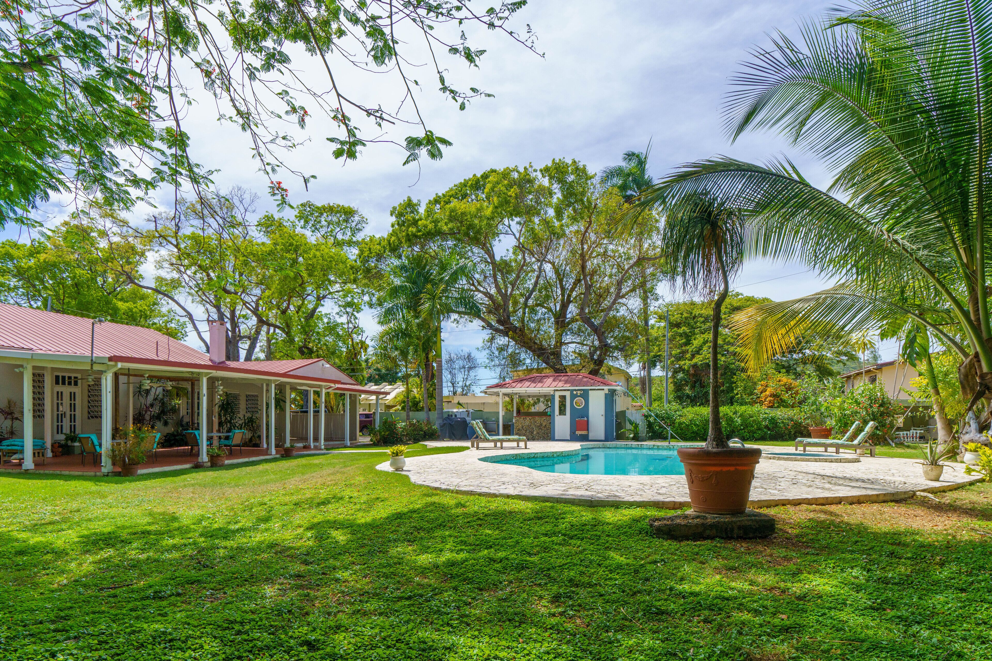 Un'area piscina con zona relax coperta, un piccolo edificio e vegetazione lussureggiante.