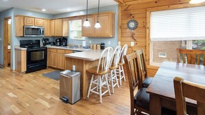 A kitchen with wooden cabinets, a stainless steel microwave, a black stove, and a wooden dining table with chairs.
