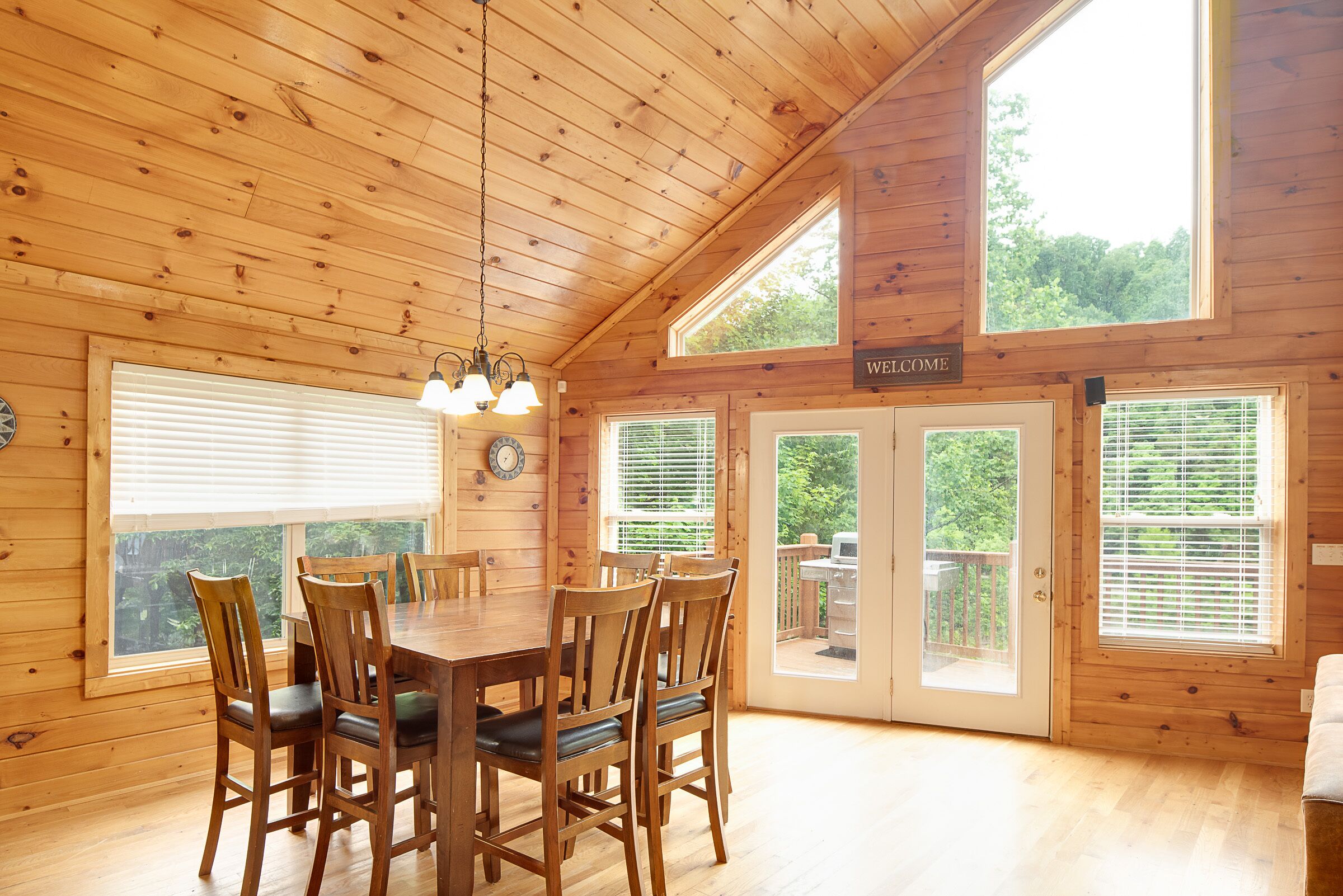 L’intérieur d’un chalet en bois, avec une table à manger, des chaises, une horloge et une pancarte indiquant « BIENVENUE ».