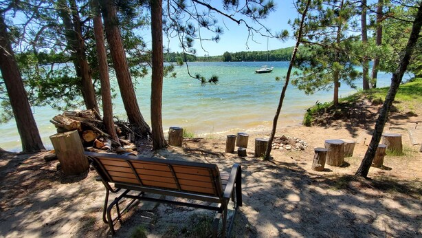 A bench in a forested area with a lake and a boat in the distance.