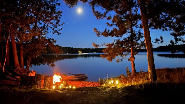 A lakeside campsite with a campfire, a boat, and a 'Swim with caution' sign. - Lakefront-Semi Rustic Cabin-8.5 acres.  Woods and lake, nature at its finest! (Frederic)