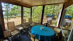 A covered outdoor seating area with a table and chairs, overlooking a natural landscape.
