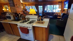 A kitchen with a stove, microwave, and refrigerator, wooden cabinets, and a dining area with a couch and table.