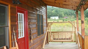 A wooden cabin with a porch, a red door, and a bench.
