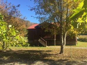 Une cabane rustique en bois, avec un toit rouge, une terrasse en bois et un escalier menant à l’entrée.