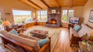 Una sala de estar acogedora con chimenea de piedra, muebles de madera y ventanas amplias que dan al exterior.