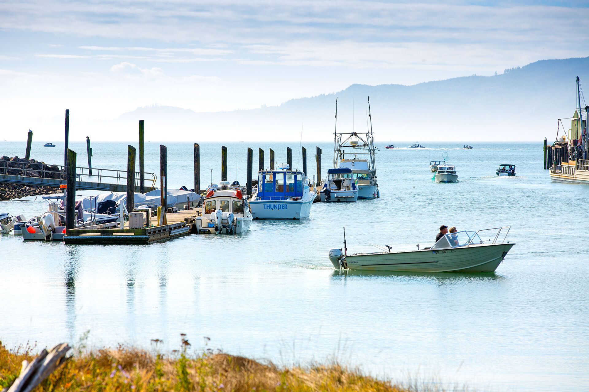 A marina with several boats docked, a pier with a bridge, and a calm sea.
