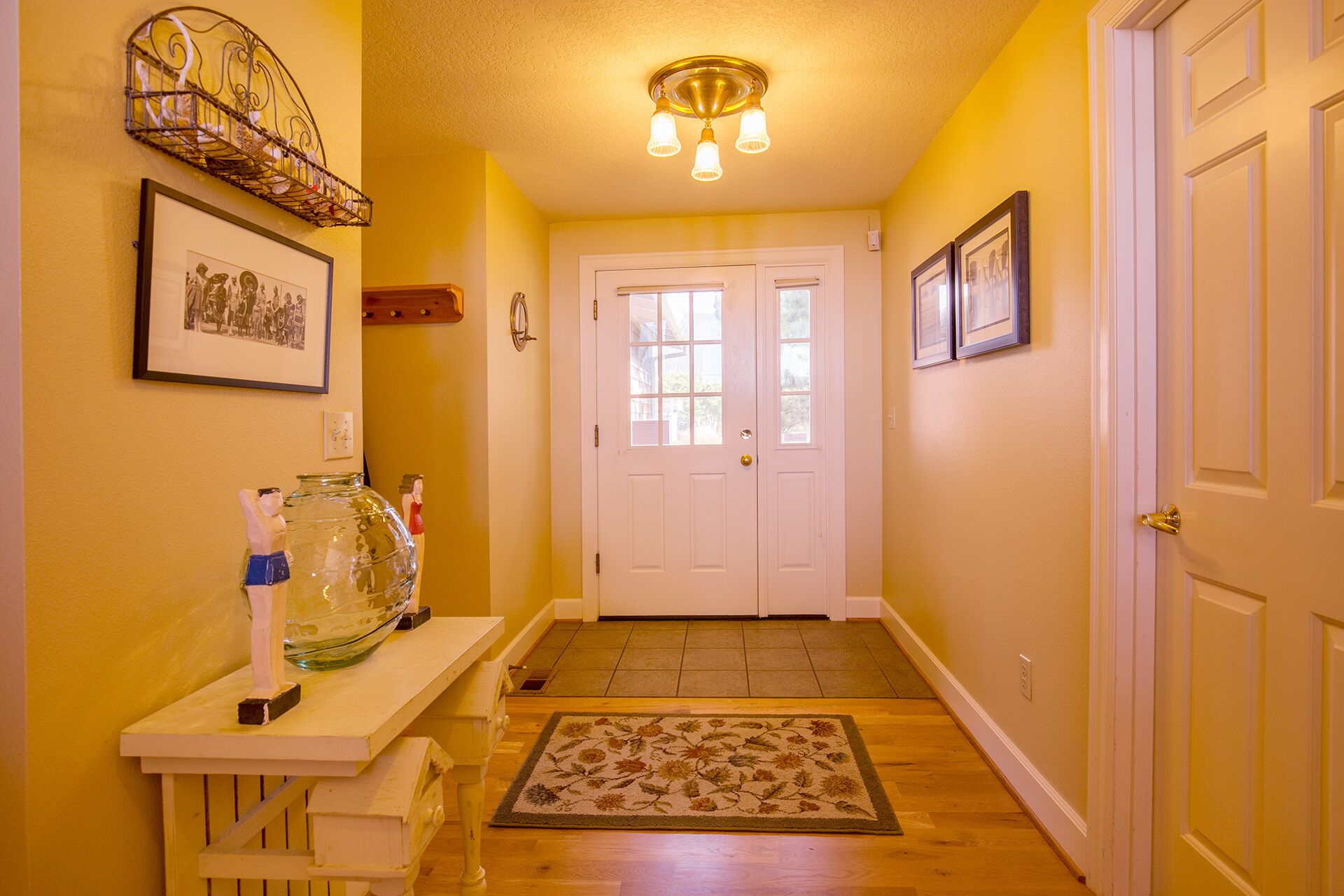 A hallway with a white door, a glass fishbowl on a wooden bench, and a patterned rug on the floor.