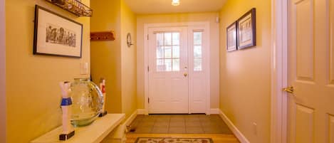 A hallway with a white door, a glass fishbowl on a wooden bench, and a patterned rug on the floor.