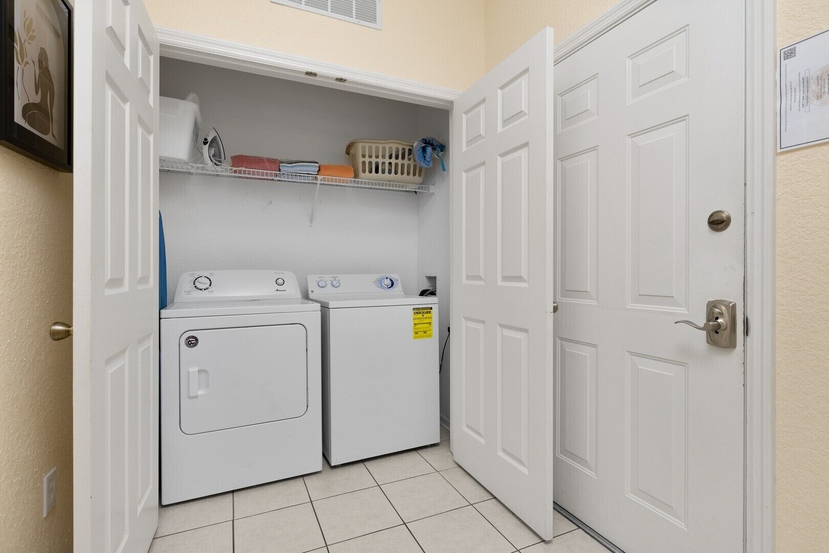 A laundry room with two white washers and dryers, a shelf with laundry supplies, and a door with a lock.
