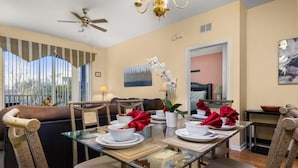 A dining area with a glass table set for four, surrounded by upholstered chairs.