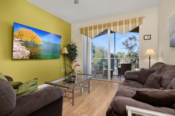A living room with a sofa, a glass coffee table, and a painting of a landscape.