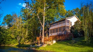 Ein Haus mit einer großen, von Mückennetzen geschützten Veranda, umgeben von Bäumen und einem Bach.