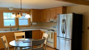 A kitchen with wooden cabinets, a stainless steel refrigerator, a dining table with chairs, and a patterned rug. - Great Location Next to Fishtown in Leland (Leland)