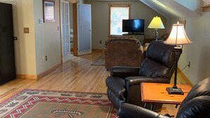 A living room with a black leather sofa, a wooden coffee table, a patterned rug, a television, and a window with blinds. - Great Location Next to Fishtown in Leland (Leland)