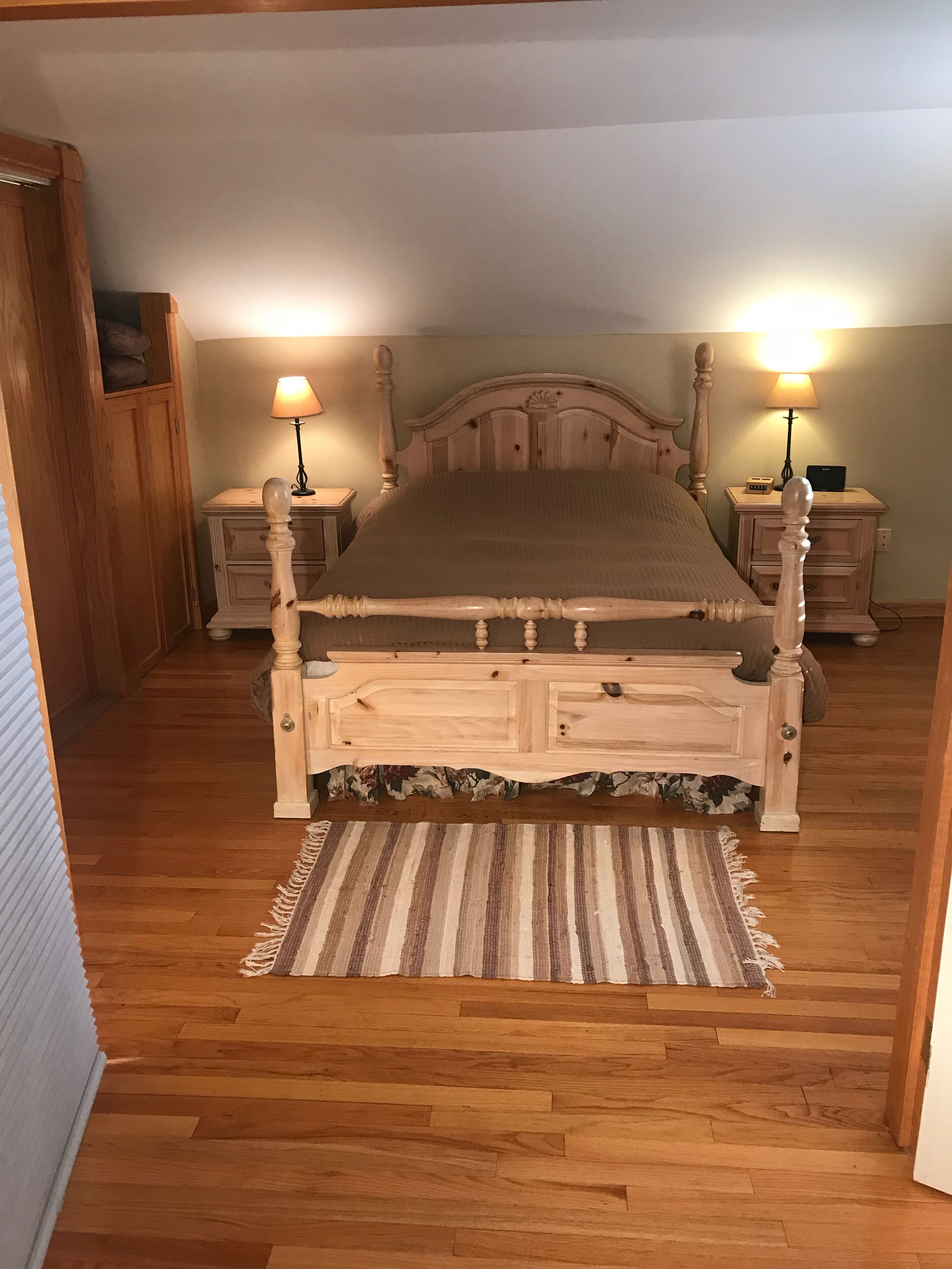 A bedroom with a wooden bed, two bedside tables, a nightstand, a wooden wardrobe, and a striped rug.