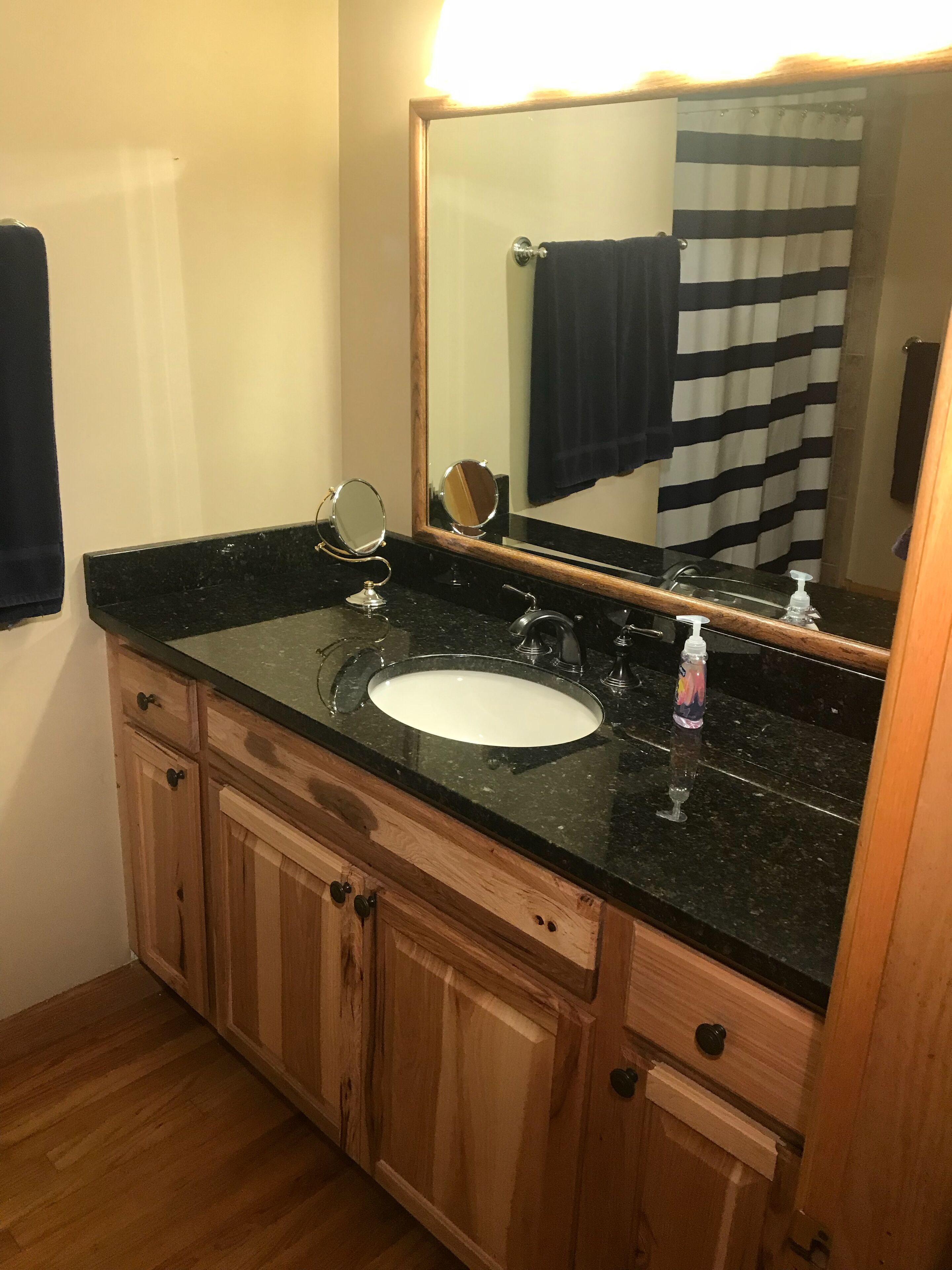 Une salle de bain avec un comptoir en granit noir, un lavabo blanc, un miroir et des armoires en bois.
