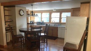 A kitchen with wooden cabinets, a dining table with chairs, a refrigerator, and a clock on the wall. - Great Location Next to Fishtown in Leland (Leland)