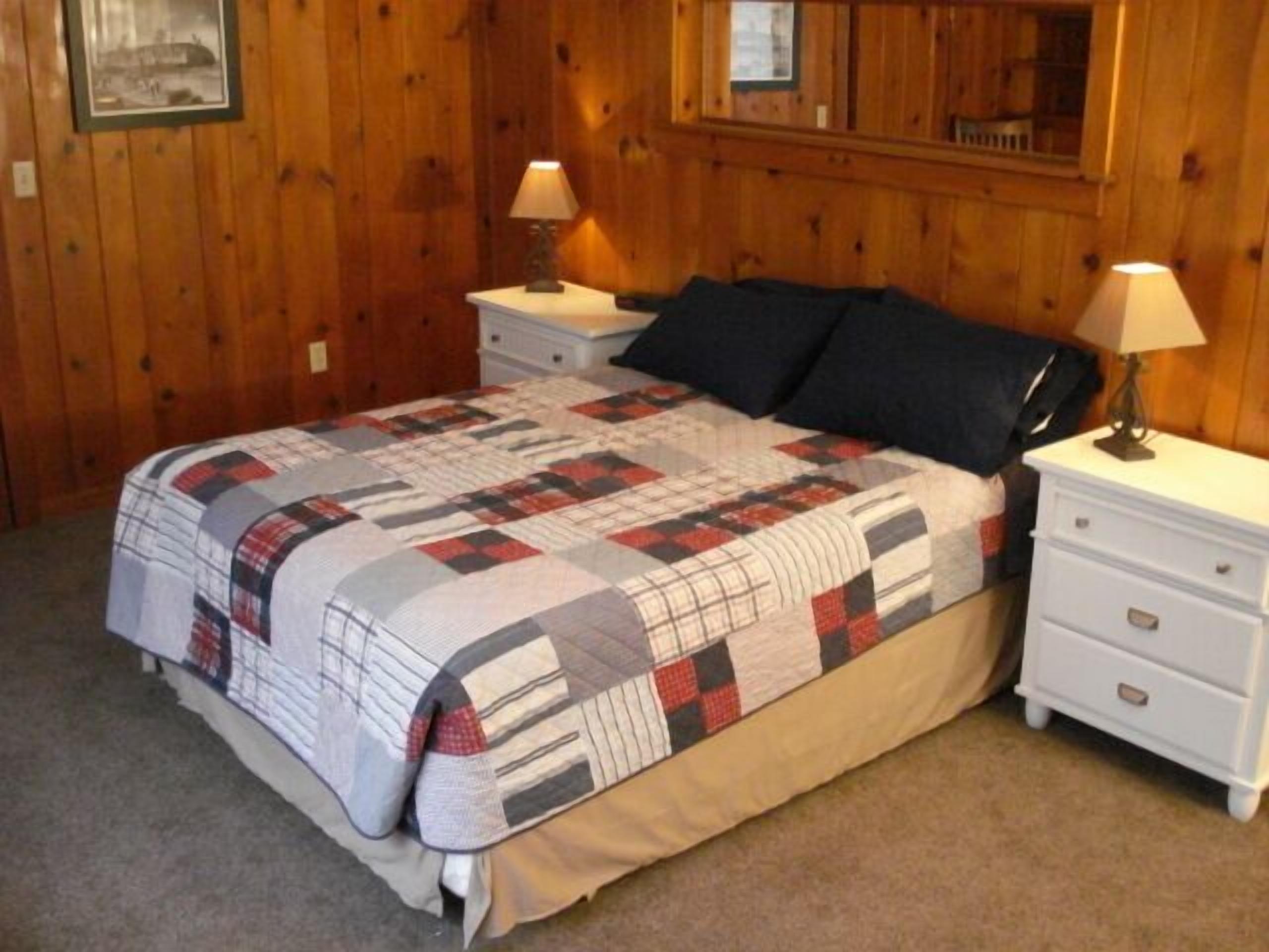 A bedroom with a bed, two nightstands, a mirror, and a quilt.