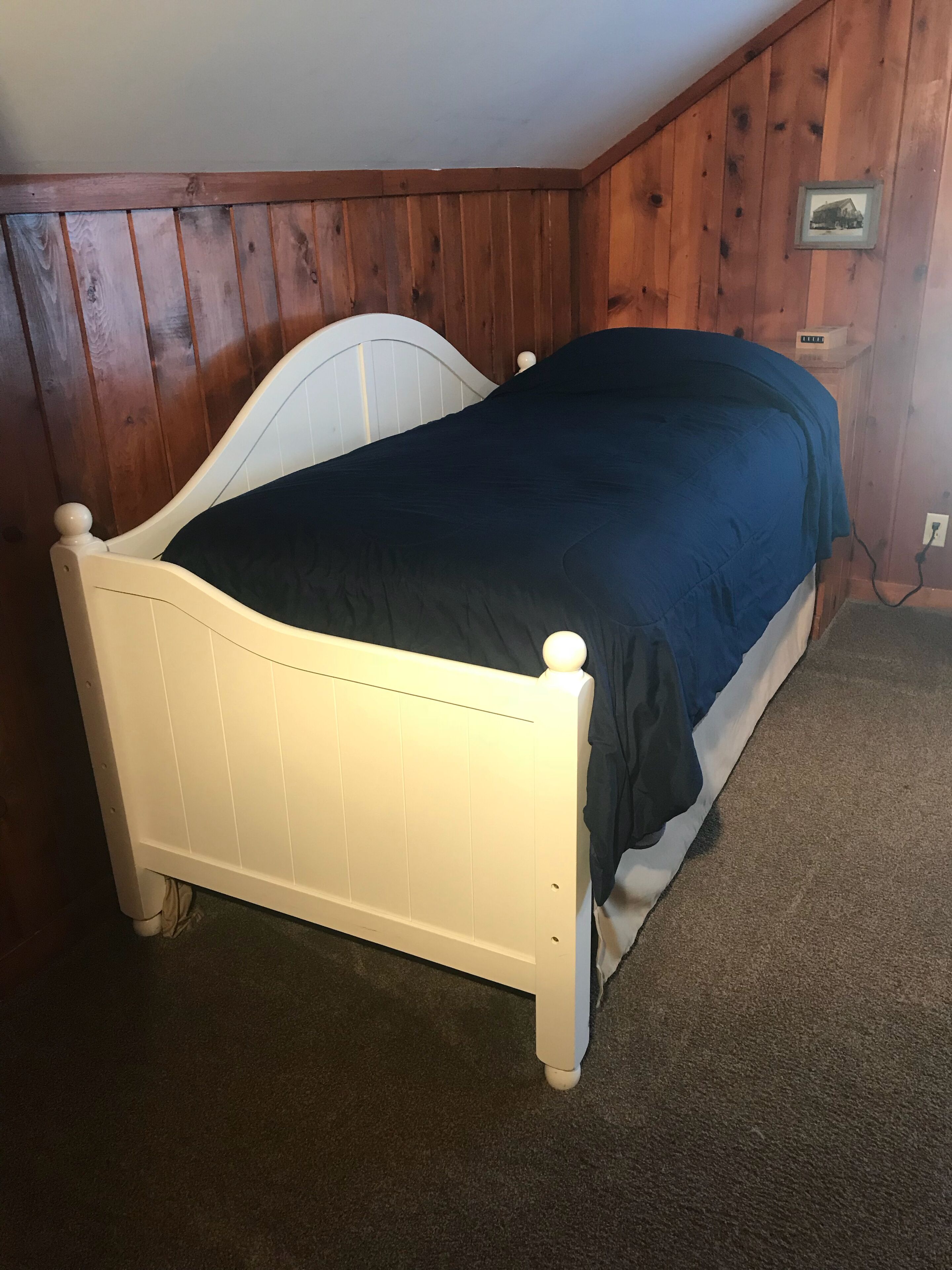 A single bed in a room with wooden paneling on the walls.