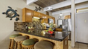 A kitchen with wooden cabinets, a black countertop, and a central island with stools.