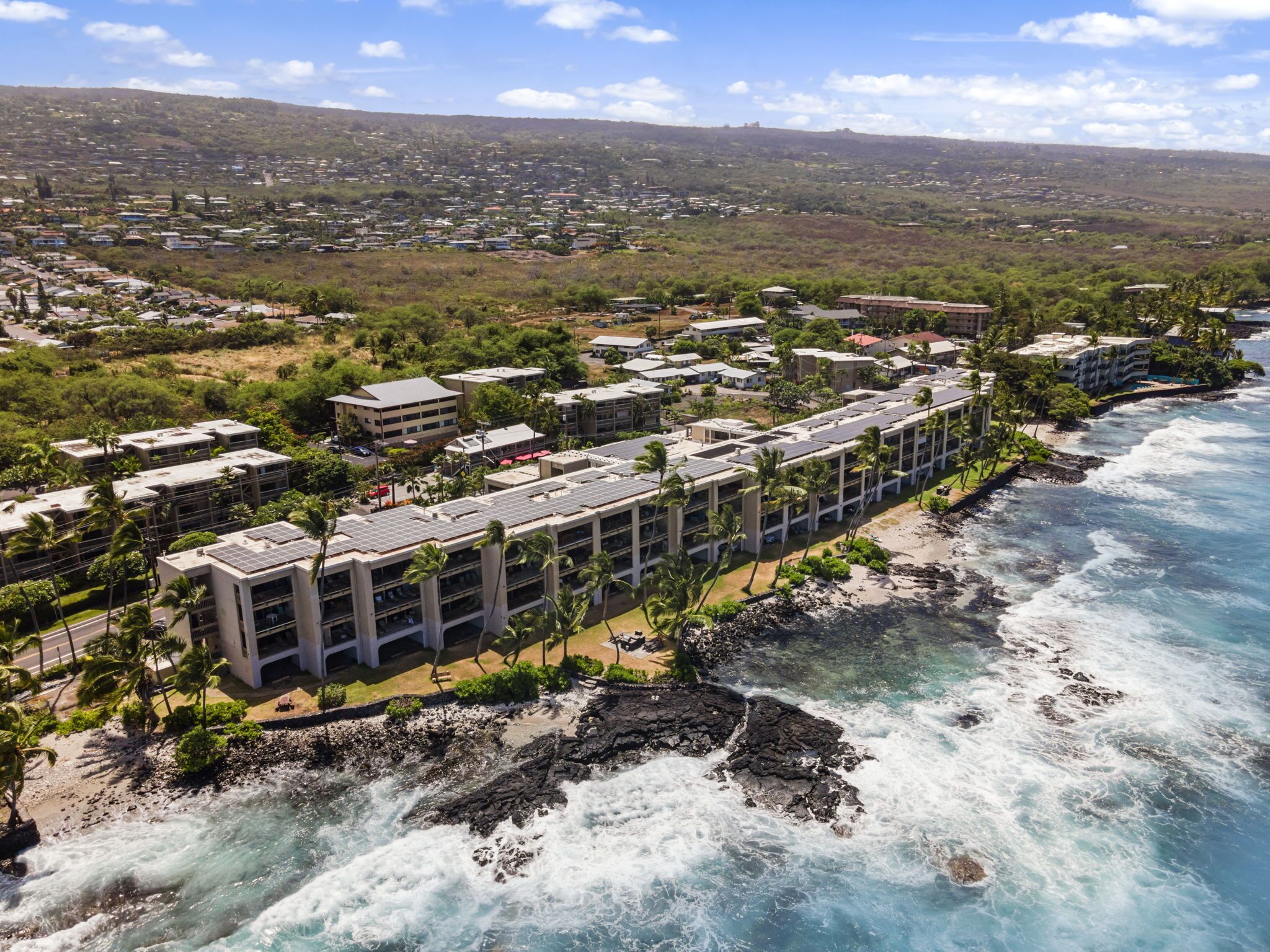 An aerial view of a coastal hotel with multiple buildings, a beachfront, and a rocky shoreline.