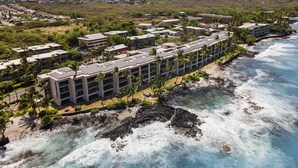 An aerial view of a coastal hotel with multiple buildings, a beachfront, and a rocky shoreline.