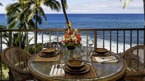A dining table set for four with a view of the ocean and palm trees.