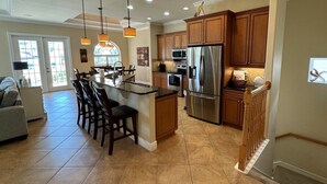 A kitchen with a central island, wooden cabinets, stainless steel appliances, and a dining area with chairs. - 4 King beds and En Suite Bathrooms - Ocean & Lake view, Elevator, 2 heated pools (Palm Coast)