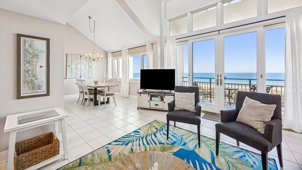 Ein geräumiges Wohnzimmer mit großem Fernseher, einem Essbereich und einem Balkon mit Meerblick.