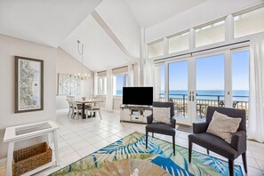 Un salón amplio con televisor grande, comedor y balcón con vista al océano.
