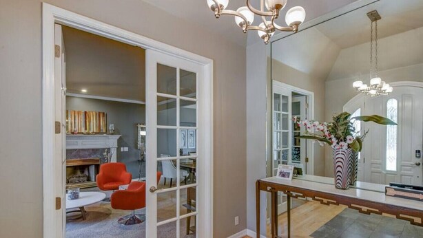 A room with a wooden floor, a red chair, a white table, and a mirror reflecting a door and a plant.
