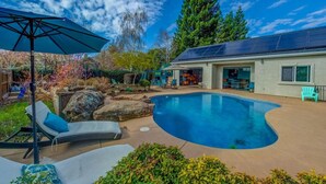 A backyard with a swimming pool, a covered patio, and a house with solar panels.