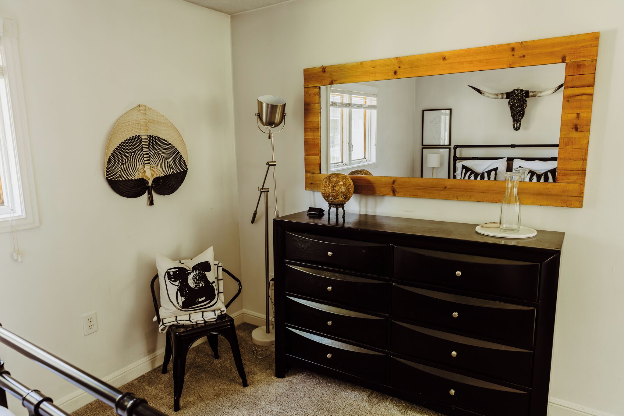 A room with a wooden dresser, a mirror with a cow skull, a lamp, and a chair with patterned cushions.