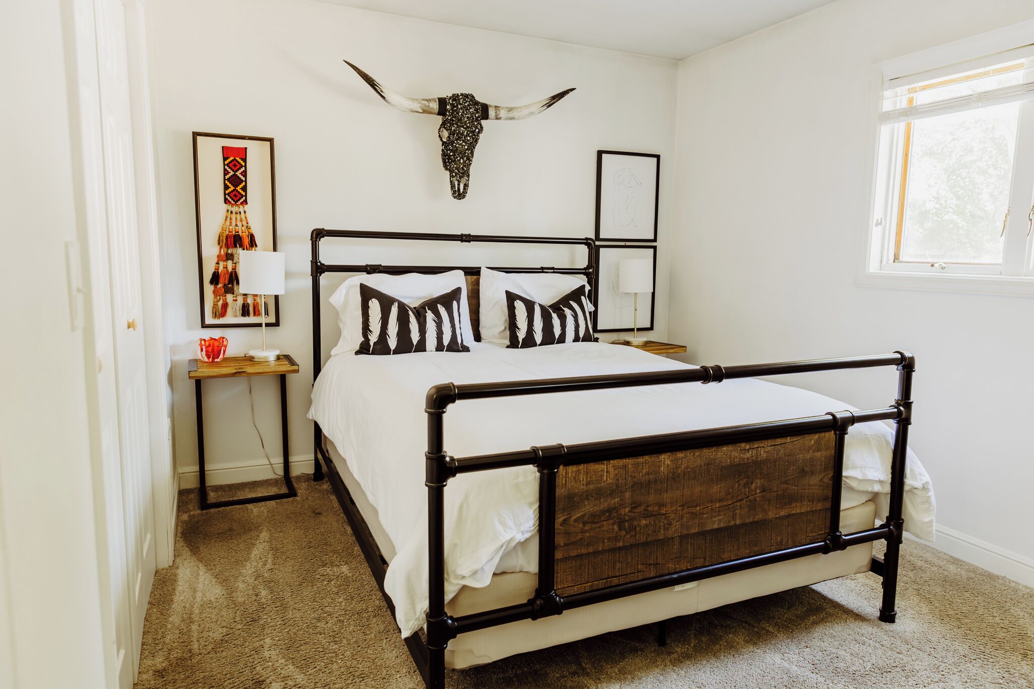 Une chambre à coucher avec un lit, des tables de chevet, une lampe, un crâne accroché au mur et une fenêtre.