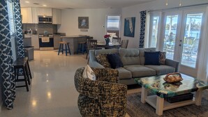 A modern living room with a sofa, chairs, a coffee table, and a kitchen in the background.