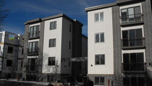 Ein mehrstöckiges Wohngebäude mit modernem Design, das Backstein und weiße Fassadenverkleidung kombiniert, viele Fenster hat und einen sichtbaren Hydranten auf dem Bürgersteig zeigt.
