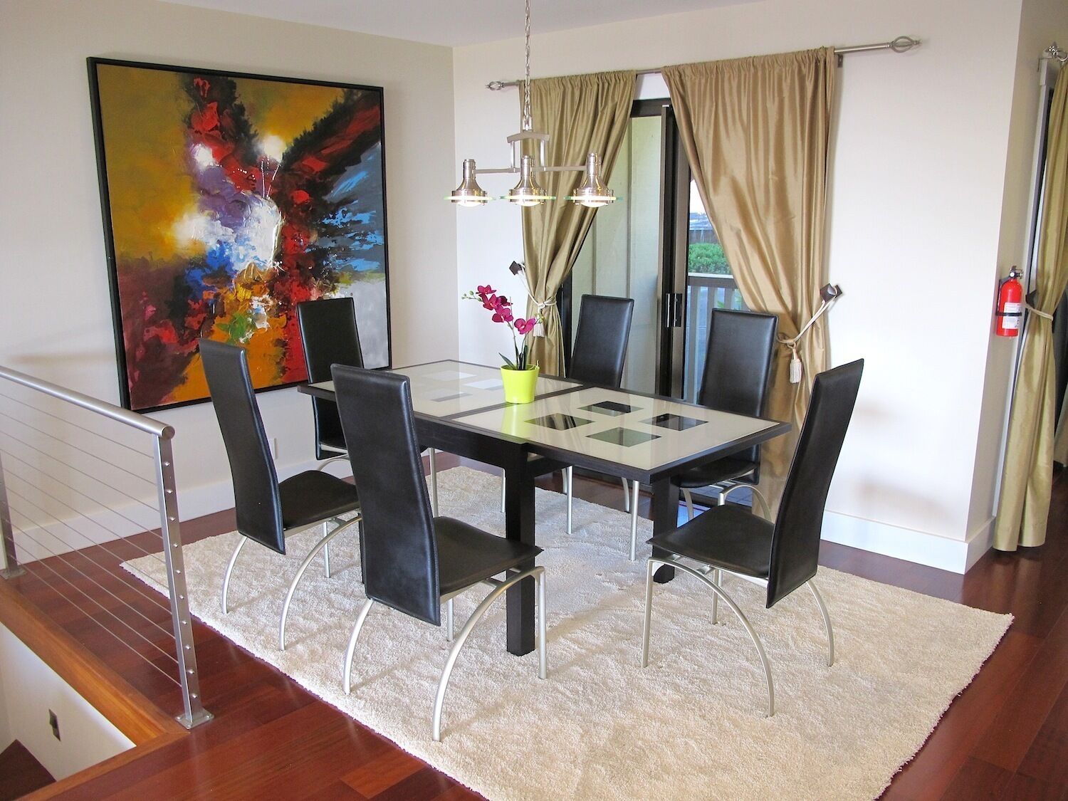 Un'elegante sala da pranzo con un tavolo in vetro, sedie nere, un vaso giallo e un grande quadro astratto appeso alla parete.