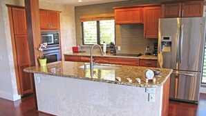 Una cocina con encimeras de granito, electrodomésticos de acero inoxidable, armarios de madera y una isla grande con fregadero.