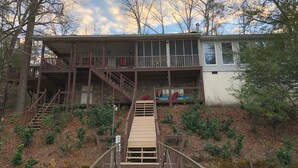 A two-story wooden cabin with a wooden deck leading to a stone staircase.